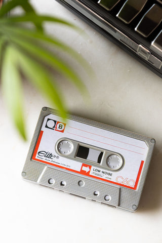 The Party Mix Cassette Tape Storage Tin seen from above, styled on a marble surface with a plant and another storage tin.