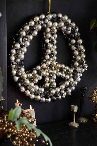 The Peace Wreath hanging on a black wall, styled with lit candles, decorative accessories and some greenery.