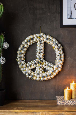 The Peace Wreath hung on a dark wood wall above a wooden unit styled with a wall art print and gold pillar candles.