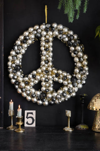 The Peace Wreath styled on a black wall, surrounded by various home accessories and greenery.