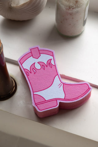 The Pink Cowboy Boot Sponge styled with bathroom props on a white surface.