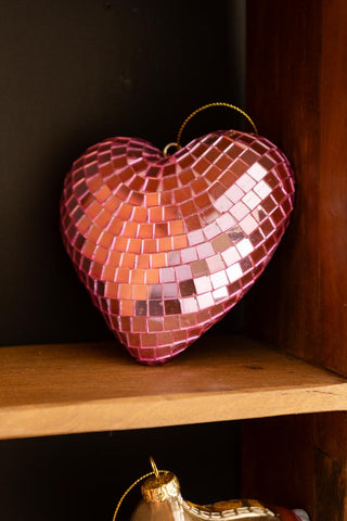 The Pink Disco Heart Christmas Tree Decoration displayed on a wooden shelf.