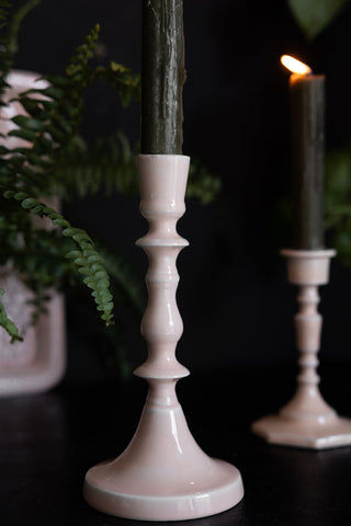 Close-up shot of the Tall Pink Enamel Cast Style Candlestick Holder displayed together with the short version, both with candles inside, styled with plants in the background.