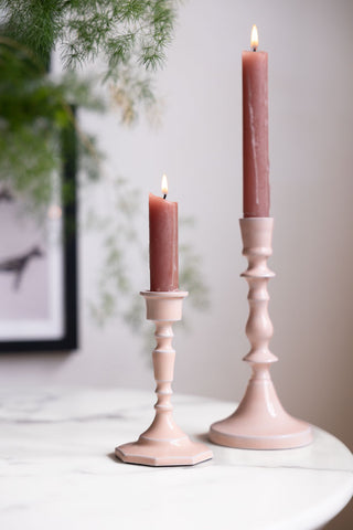 The Short and Tall Pink Enamel Cast Style Candlestick Holders displayed with lit pink candles inside, styled with a plant and black frame in the background.