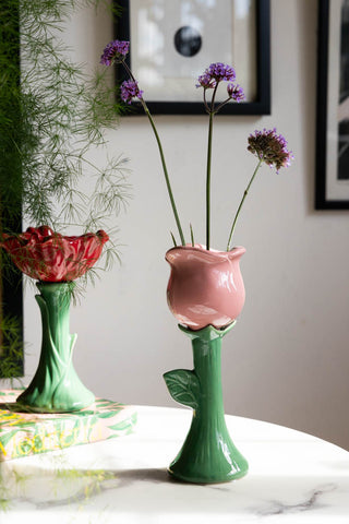 The Pink Flower Earthenware Single Stem Vase styled with greenery inside, displayed on a white marble surface with other home accessories.