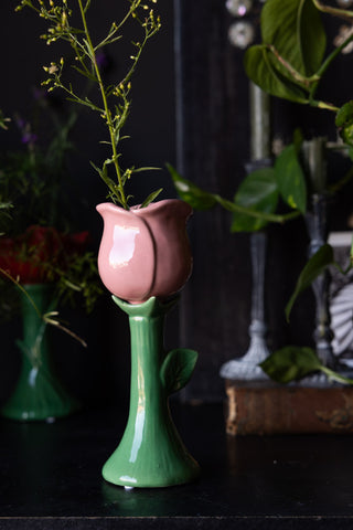 The Pink Flower Earthenware Single Stem Vase styled with a stem of greenery inside, with a plant and home accessories in the background.