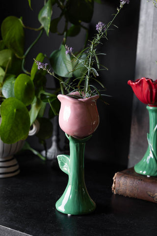 The Pink Flower Earthenware Single Stem Vase styled with the red version in the background, with various plants and greenery.