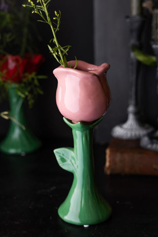 The Pink Flower Earthenware Single Stem Vase styled with greenery inside, displayed on a black surface with other home accessories.