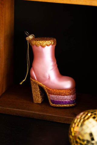 The Pink Glass Heeled Boot Christmas Tree Decoration styled on wooden shelf, with a gold disco ball ornament to the side of the shot.