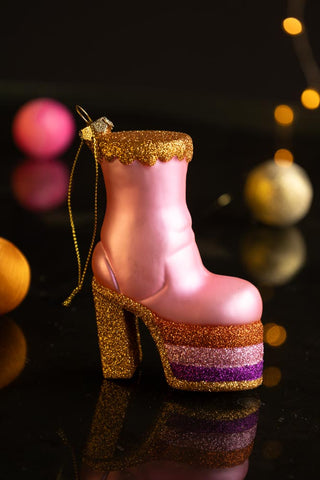 The Pink Glass Heeled Boot Christmas Tree Decoration styled on a dark surface with baubles and fairy lights in the background.