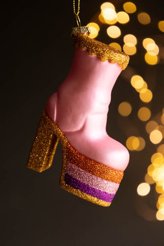 The Pink Glass Heeled Boot Christmas Tree Decoration hanging in front of a dark background with fairy lights.