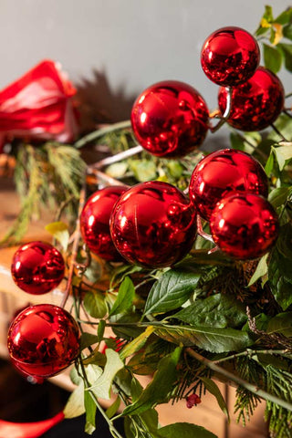 Close-up image of the Shiny Red Bauble Spray on a green leaf garland on a wooden mantlepiece.