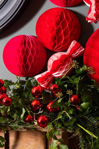 Image of the Set Of 2 Red Honeycomb Ball Decorations on top of a mantlepiece with red and pink christmas decorations.