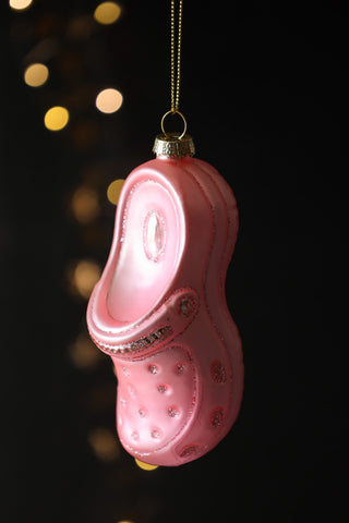 The Pink Shoe Christmas Tree Decoration styled hanging in front of a dark background with glowing lights.