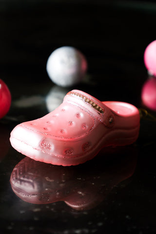 The Pink Shoe Christmas Tree Decoration styled on a dark surface with baubles in the background.