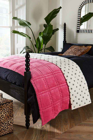 The Reversible Hot Pink Star Throw styled folded on the end of a bed.