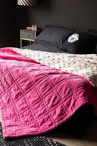 The Reversible Hot Pink Star Throw styled on a bed with black bedding.