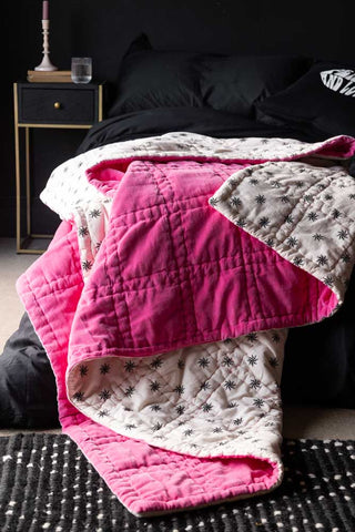 The Reversible Hot Pink Star Throw draped across the corner of a bed with black bedding.