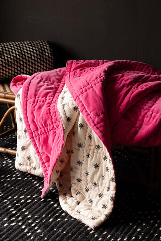 The Reversible Hot Pink Star Throw draped across a wicker bench.