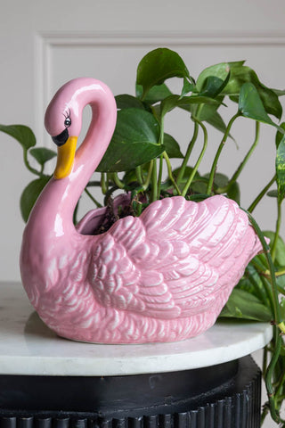 A fun and quirky swan vase on a white marble console. The vase has a green plant in it.