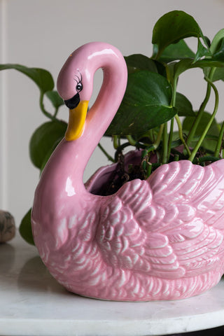 A close-up of the pink swan vase with a gold yellow beak with a green plant planted in the pot.