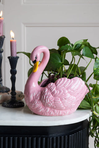 A very quirky pink swan planter with a green plant cascading down and out of the back of the vase.