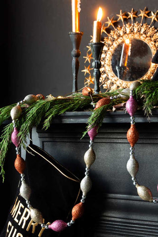 Image of the Pink & Gold Sparkle Bauble Garland styled over a black fireplace with a conifer branch.