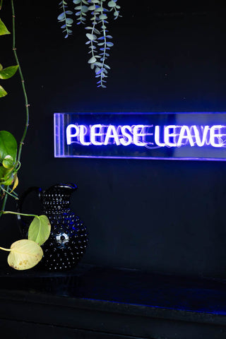 Detail shot of the Please Leave By 9pm Neon Lightbox illuminated and displayed on a black wall.