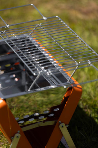 Detail shot of the Portable Suitcase BBQ - Burnt Orange displayed outdoors on some grass.