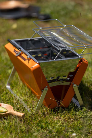 The Portable Suitcase BBQ - Burnt Orange assembled and displayed on grass in the sunshine.