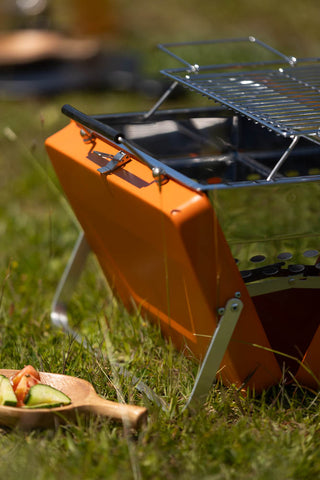 Close-up shot of the Portable Suitcase BBQ - Burnt Orange on some grass.