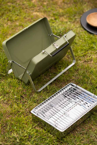 The Portable Suitcase BBQ - Khaki Green shown displayed in two separate parts on grass.