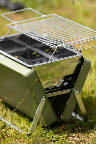 Close-up of the Portable Suitcase BBQ - Khaki Green assembled on some grass.