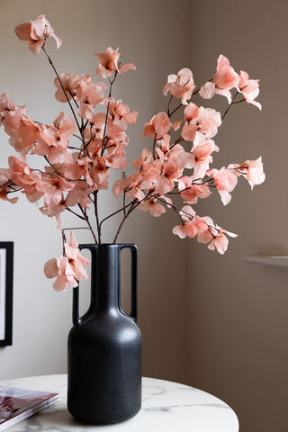 The Pretty Pink Blossom Flower Stem styled in a large vase, on a round marble table alongside some magazines.