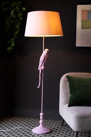 The Pretty Pink Parrot Floor Lamp with Shade switched on and styled in the corner of a room with a chair.