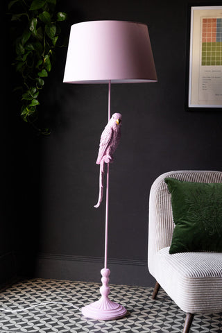 The Pretty Pink Parrot Floor Lamp with Shade styled next to a chair and cushion, with an art print and plant in the background.