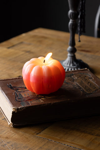 The Pink Ombre Pumpkin Candle lit and styled on a book, with a candlestick holder in the background.