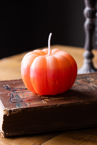 The Pink Ombre Pumpkin Candle styled on a book, on a wooden surface.