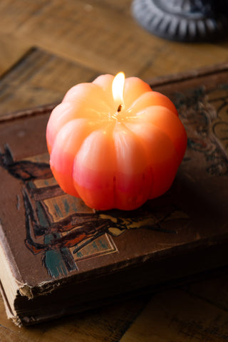 The Pink Ombre Pumpkin Candle lit and styled on a book, on a wooden surface.