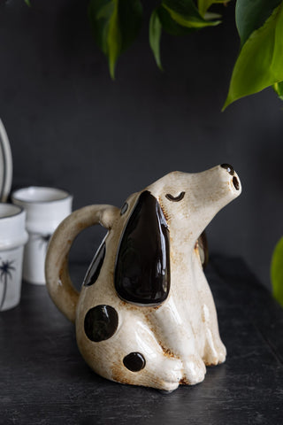 The Quirky Spotted Dog Pitcher Jug on a black surface with a plant and other accessories in the background.