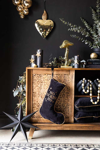 A Lifestyle image of The Merry Fuck This Black Christmas Stocking hanging in front of a leopard print unit, styled with Christmas decorations.