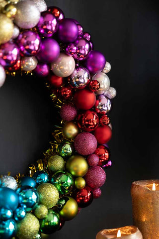 Close-up of the Rainbow Christmas Wreath hanging on a dark wall, styled above some gold candles.