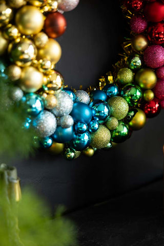 Close-up of the bottom of the Rainbow Christmas Wreath styled on a dark wall, hanging above some greenery and a candlestick holder.