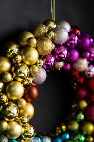 Detail shot of the Rainbow Christmas Wreath hanging on a dark wall.