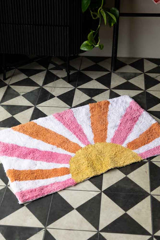 The Ray of Sunshine Tufted Cotton Bath Mat styled on a geometric floor in front of a cupboard, towel rack and plant.