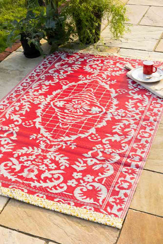 Recycled plastic red floral garden rug with a bold white pattern on a stone patio.