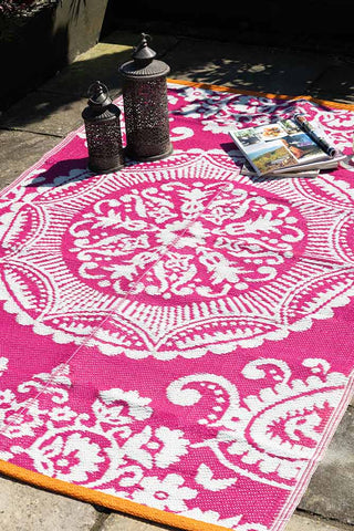 The Recycled Vintage Design Outdoor Rug in Pink styled with two lanterns and some magazines, on a patio in the sun.