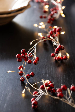 A table setting with red berries in the centre and lights turned on.