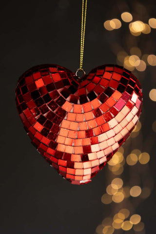 The Red Disco Heart Christmas Tree Decoration hanging in front of a dark background with fairy lights.