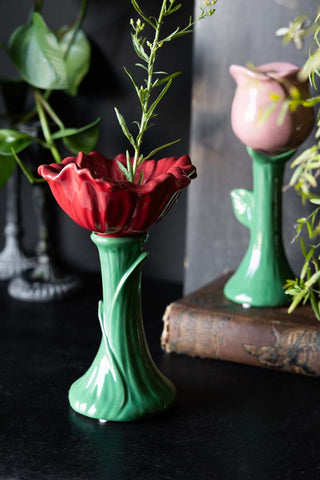 The Red Flower Earthenware Single Stem Vase on a black surface with the pink version in the background, styled with lots of greenery.